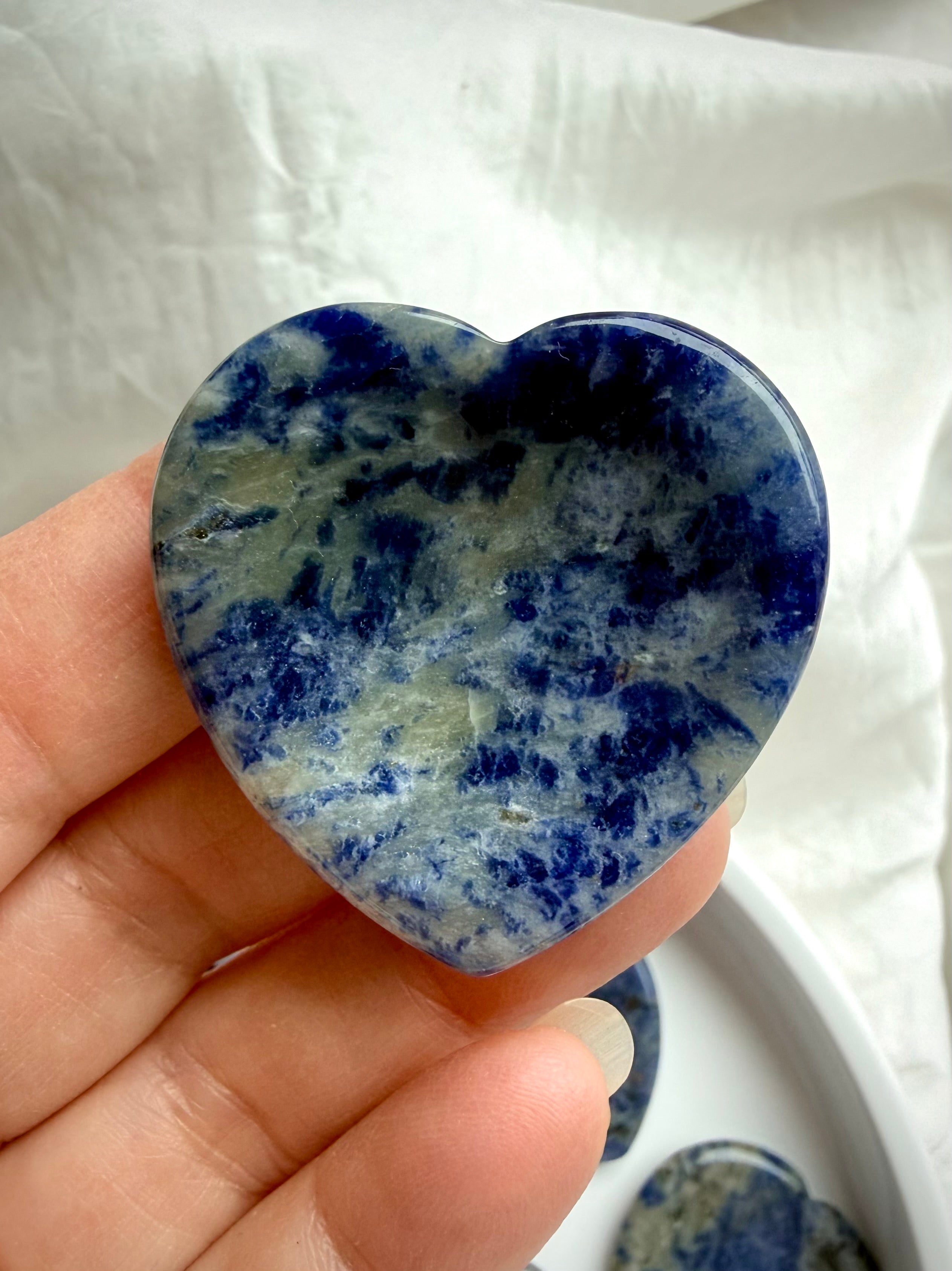 Sodalite heart worry stone held in hand showing natural blue, gray and white crystal patterns