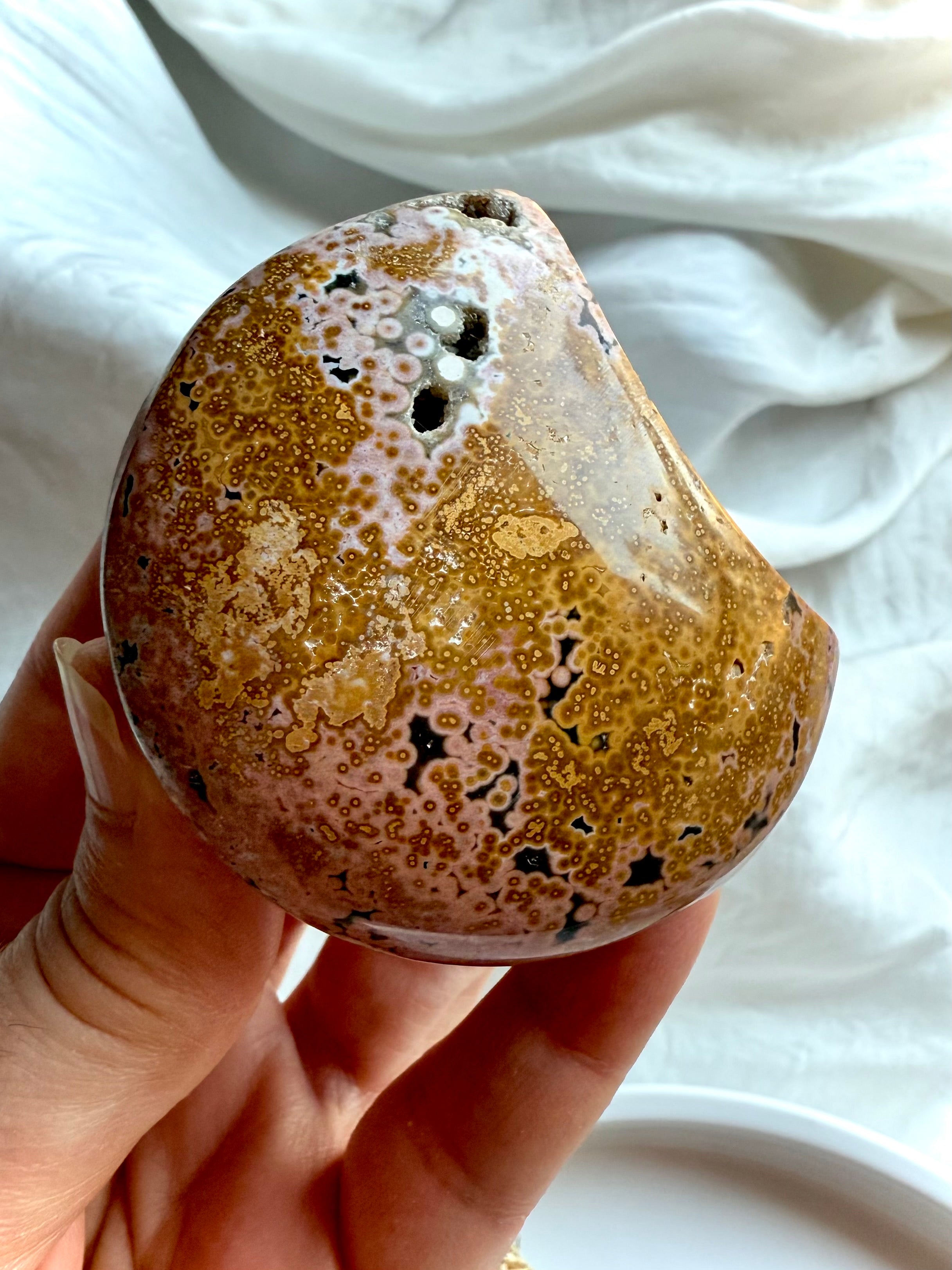 ocean jasper moon carving with peachy pink and yellow orbicular patterns held in hand, a soothing emotional healing crystal for comfort and balance