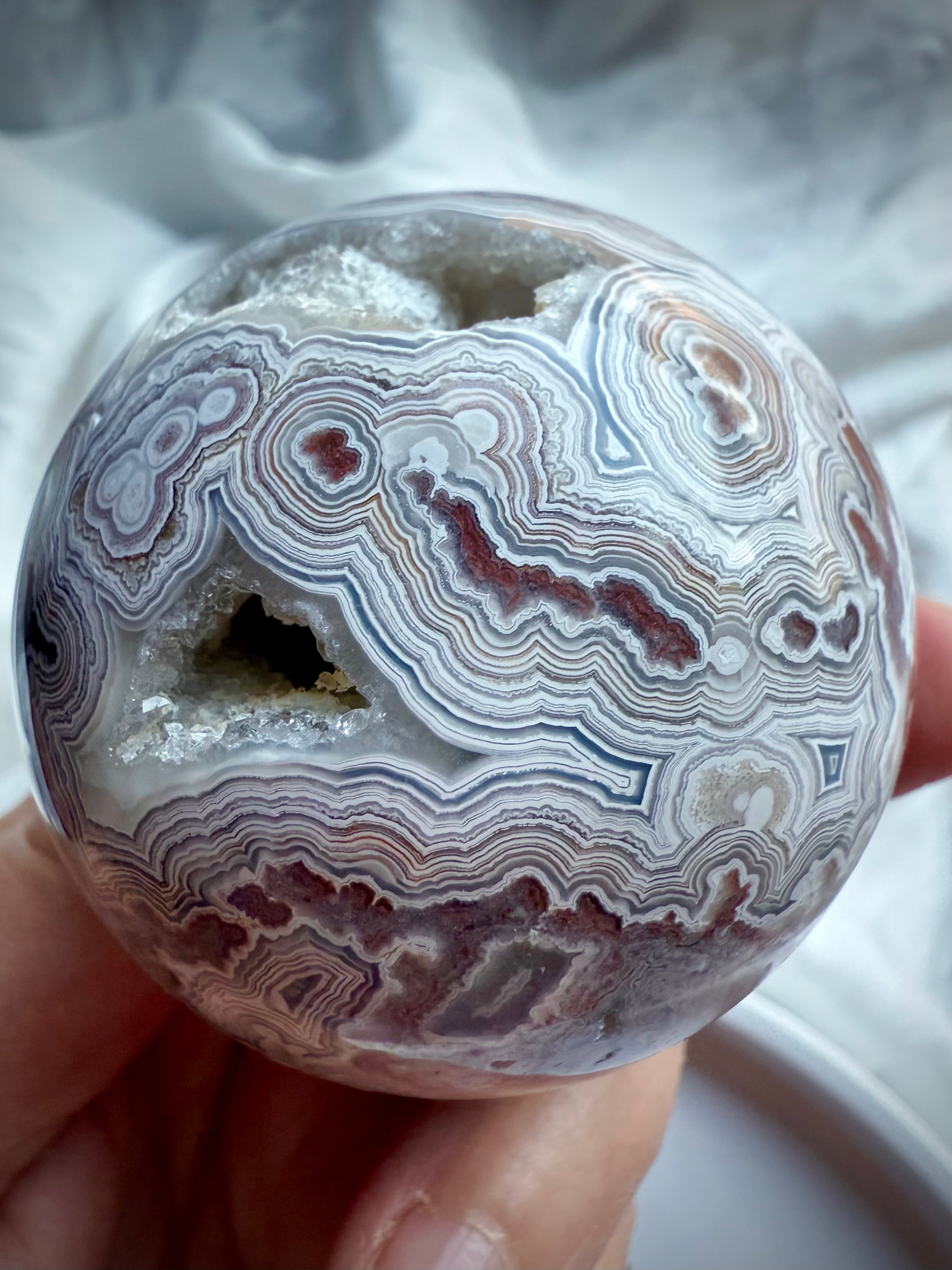 Detailed view of Crazy Lace Agate sphere with joyful swirling patterns, grounding red hues, and sparkling quartz inclusions