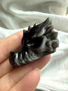 silver sheen obsidian dragon carving in hand with visible sheen effect, protective stone for transformation clarity and balance