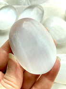 White Selenite palm stone with radiant pearlescent sheen, polished finish, and soft linear crystal texture