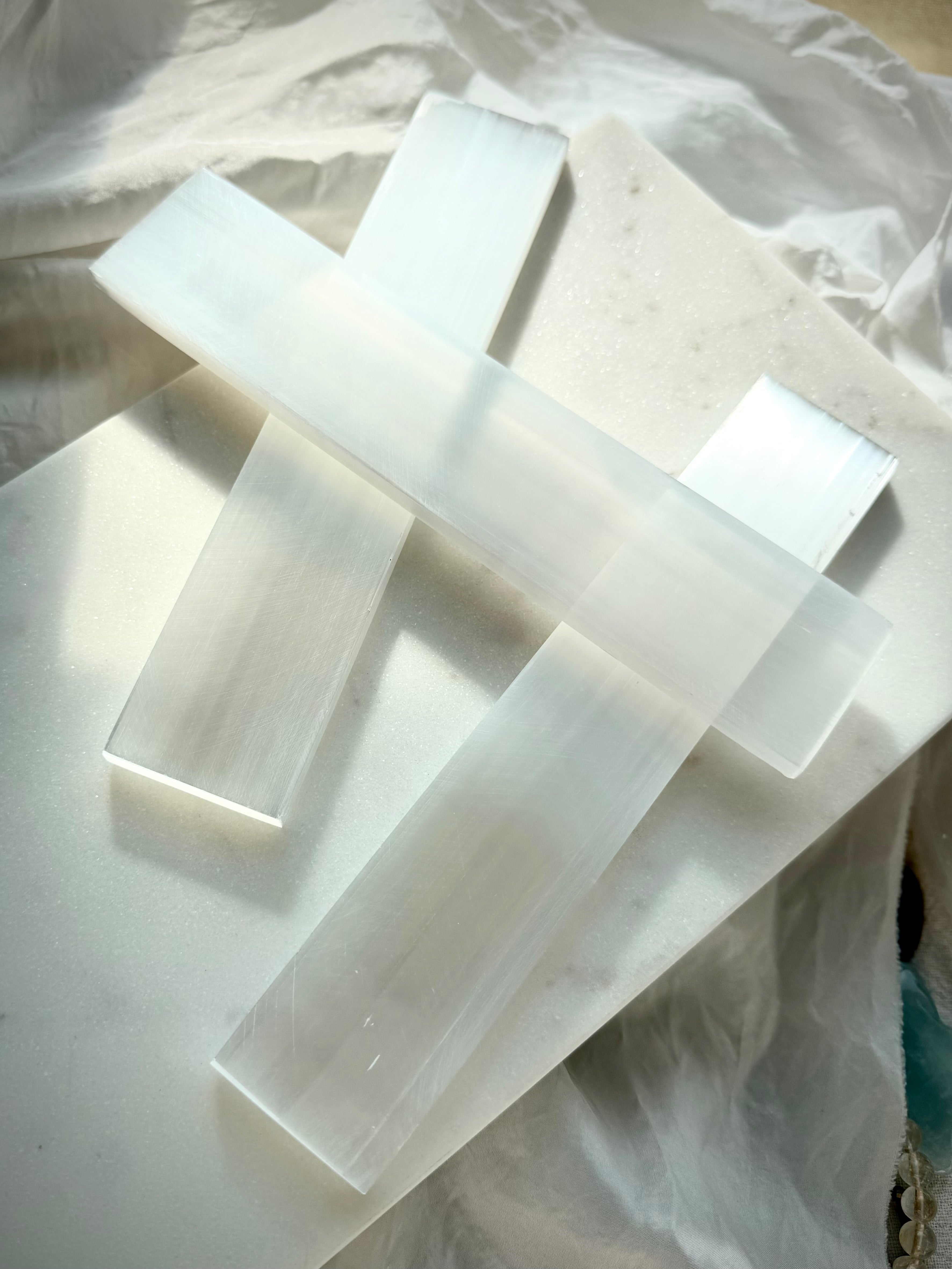 Natural Selenite charging bars arranged on soft white marble, showing smooth polished surfaces and luminous fibrous crystal texture