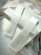 Natural Selenite charging bars arranged on soft white marble, showing smooth polished surfaces and luminous fibrous crystal texture