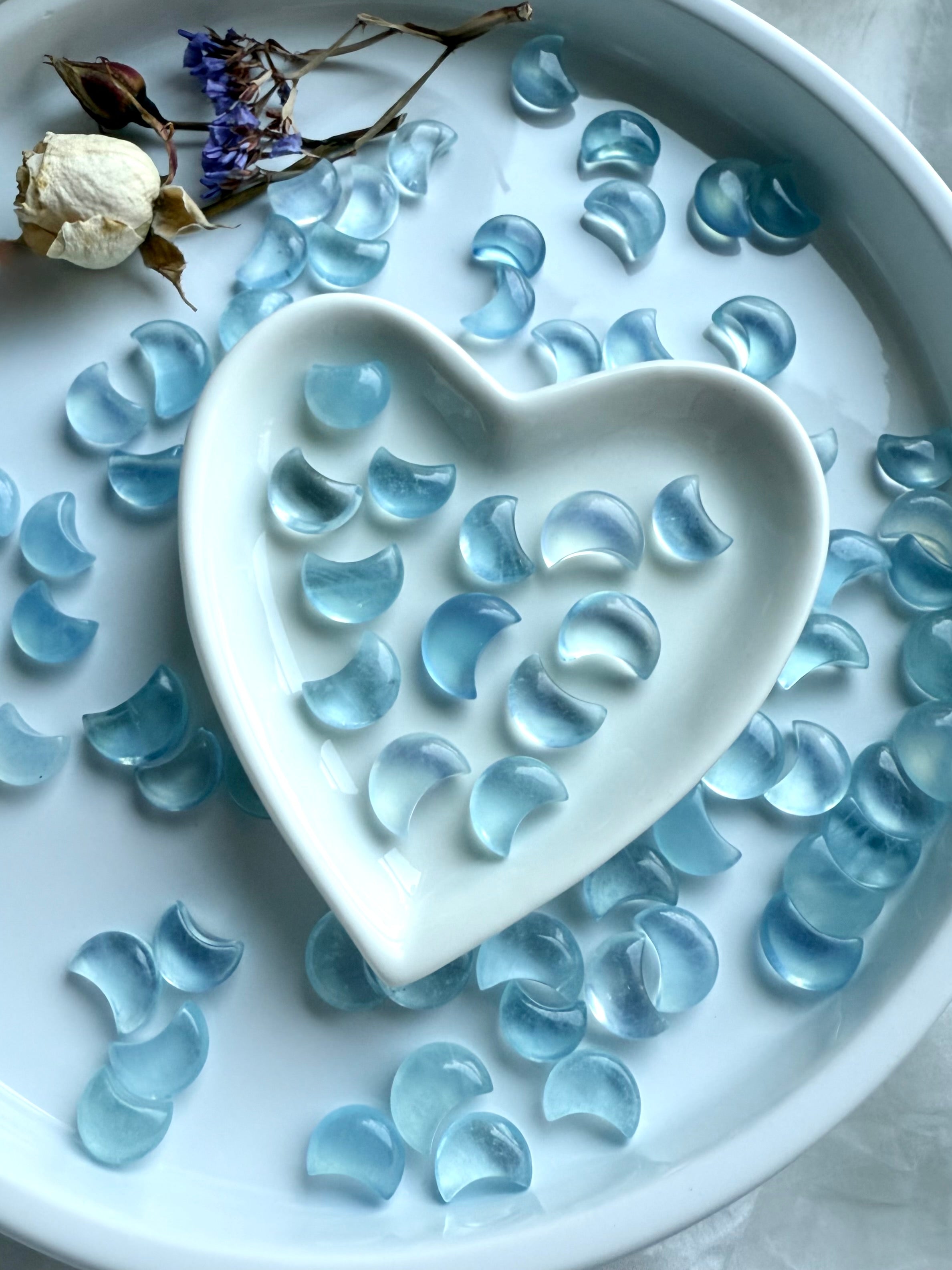 Moody crystal styling with Aquamarine moons scattered around and inside a heart dish — altar-ready gemstones for throat chakra balance and calm