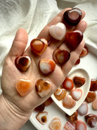 Collection of mini Carnelian heart crystals in hand, each with unique banded patterns, joyful sacral chakra healing stones