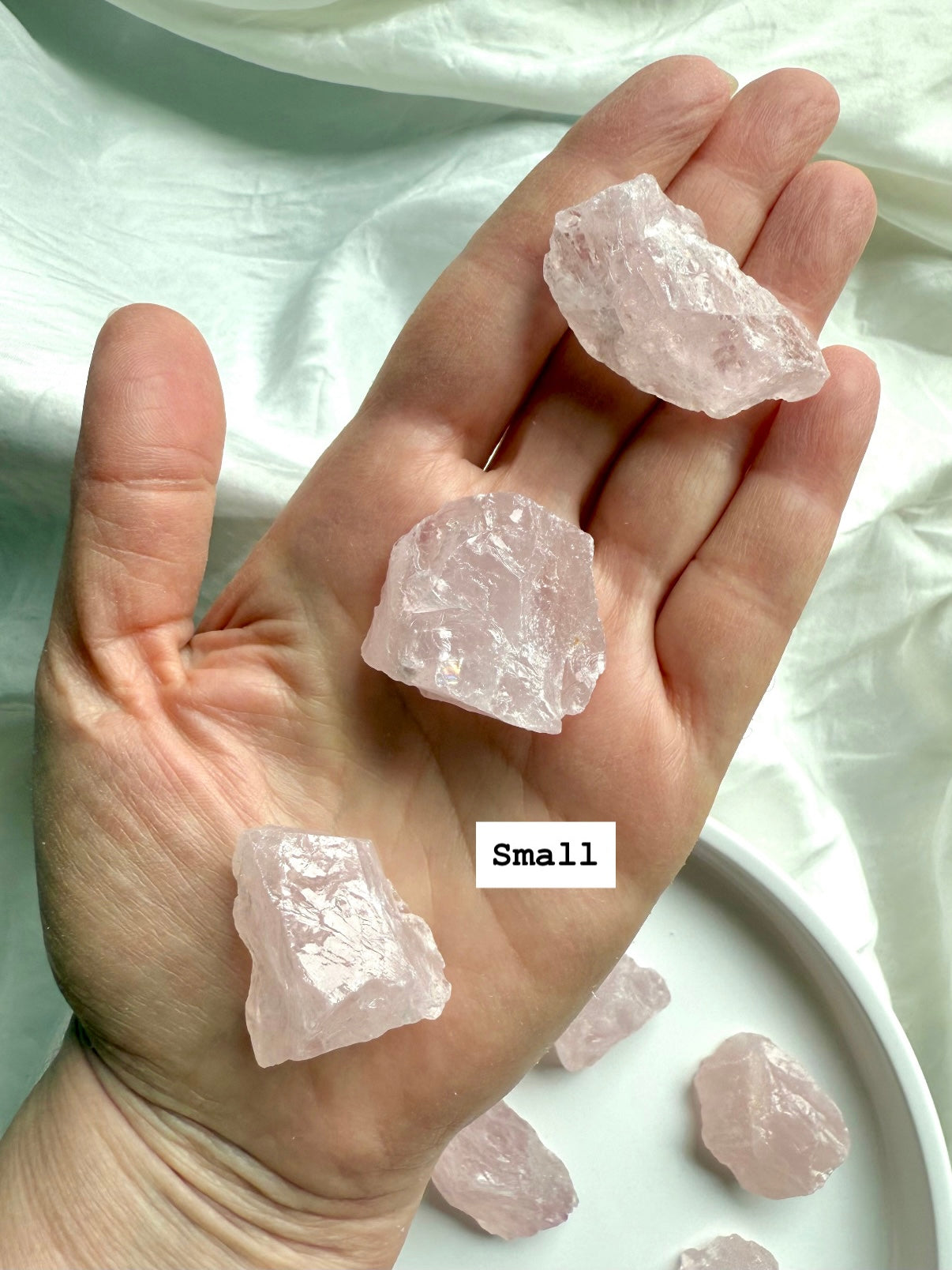 Hand holding three small raw Rose Quartz crystal chunks, pink healing stones for unconditional love and gentle energy support
