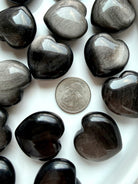 Silver Sheen Obsidian crystal hearts shown with a US quarter for scale, with glossy black surfaces and luminous silver shimmer