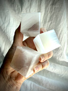 Selenite cubes held in natural light showing translucent white crystal and reflective satin spar sheen