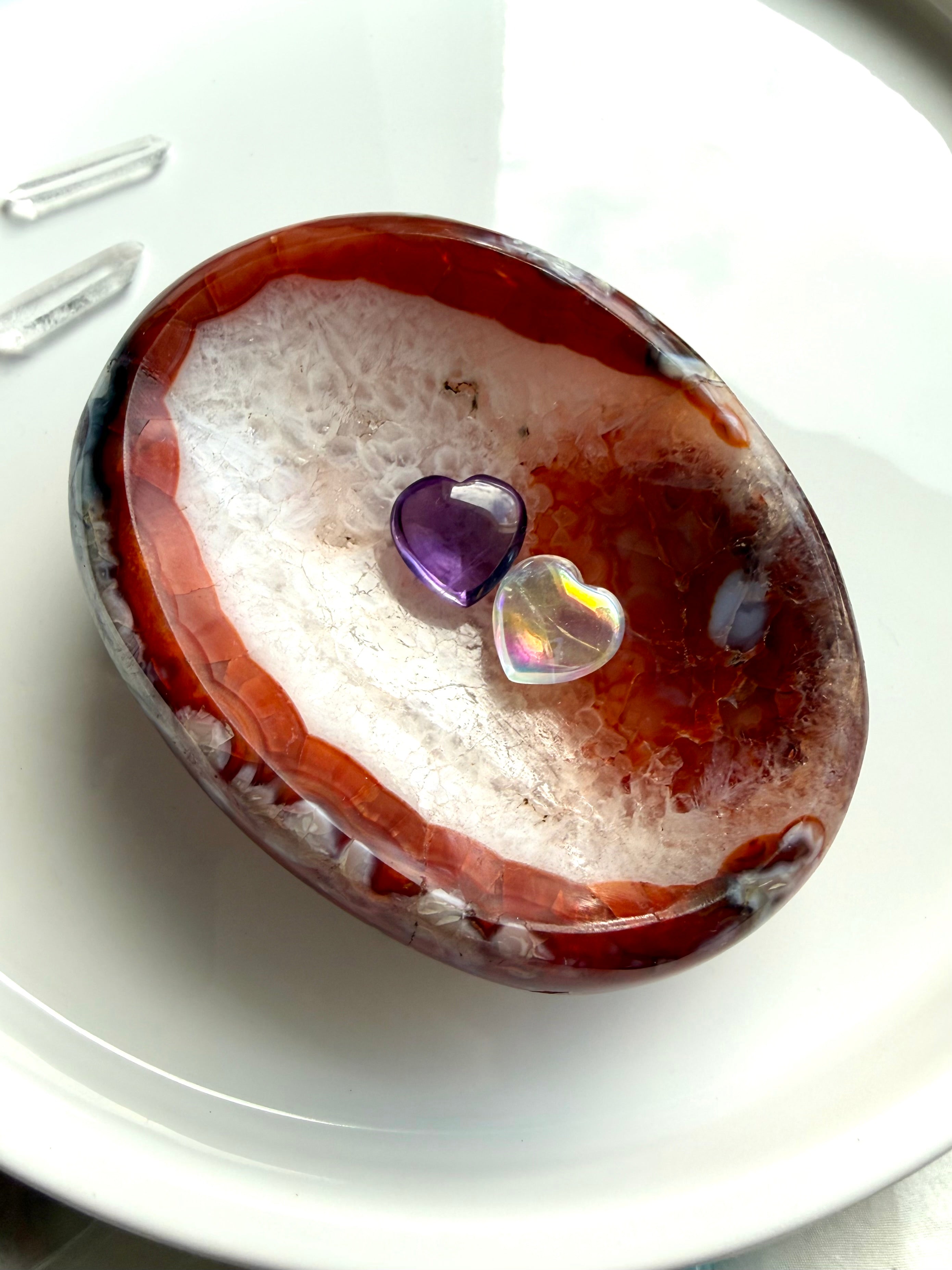 Carnelian agate bowl with druzy quartz center and translucent red edges holding 2 crystal hearts