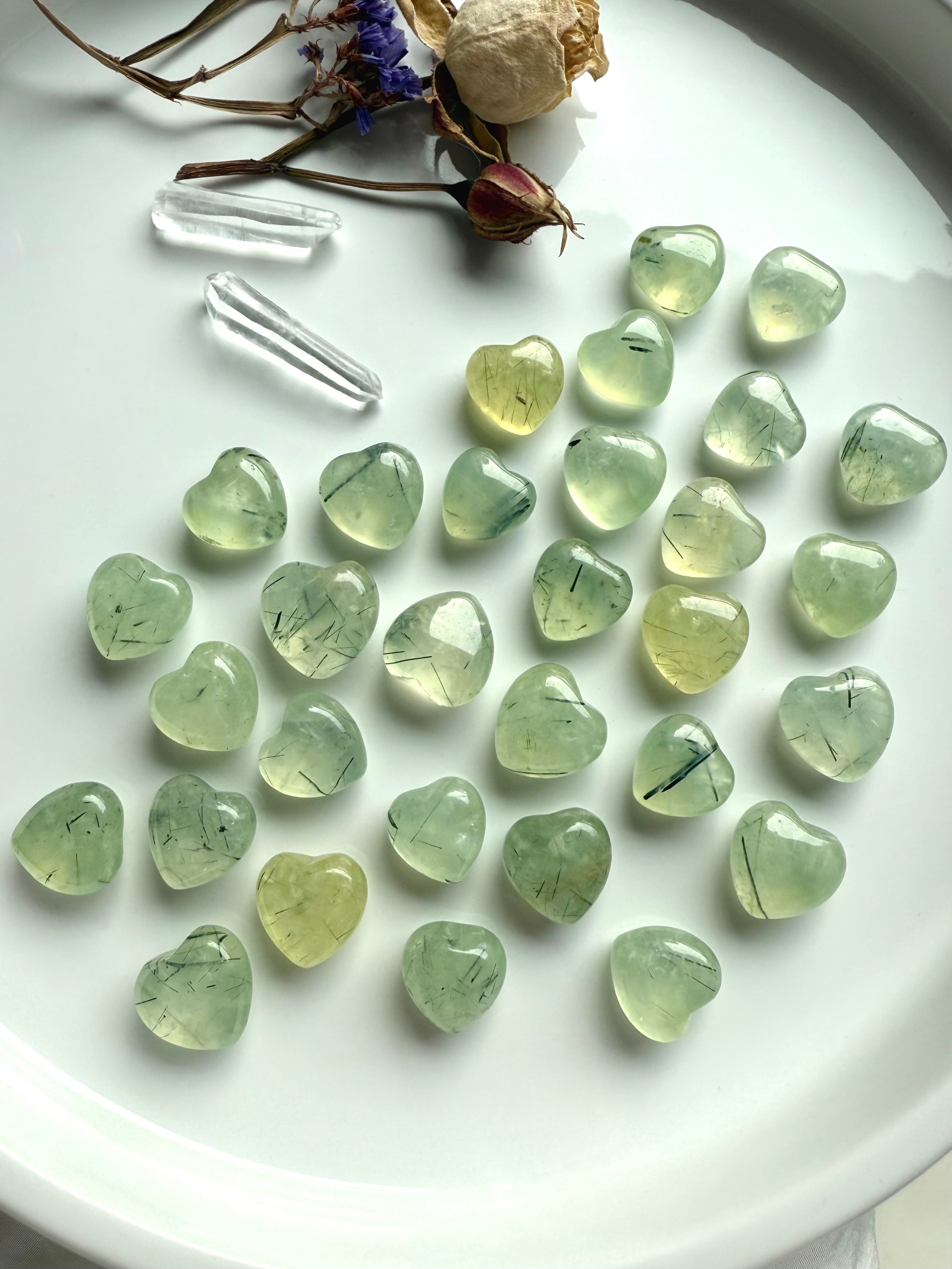 Mini Prehnite hearts with natural black tourmaline strands, arranged on a tray with an amethyst heart, quartz points, and dried flowers.