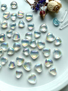 Iridescent Aura Quartz crystal hearts on a white plate with roses, statice flowers, aquamarine and quartz points – rainbow flash heart carvings for healing, love, and high-vibe energy