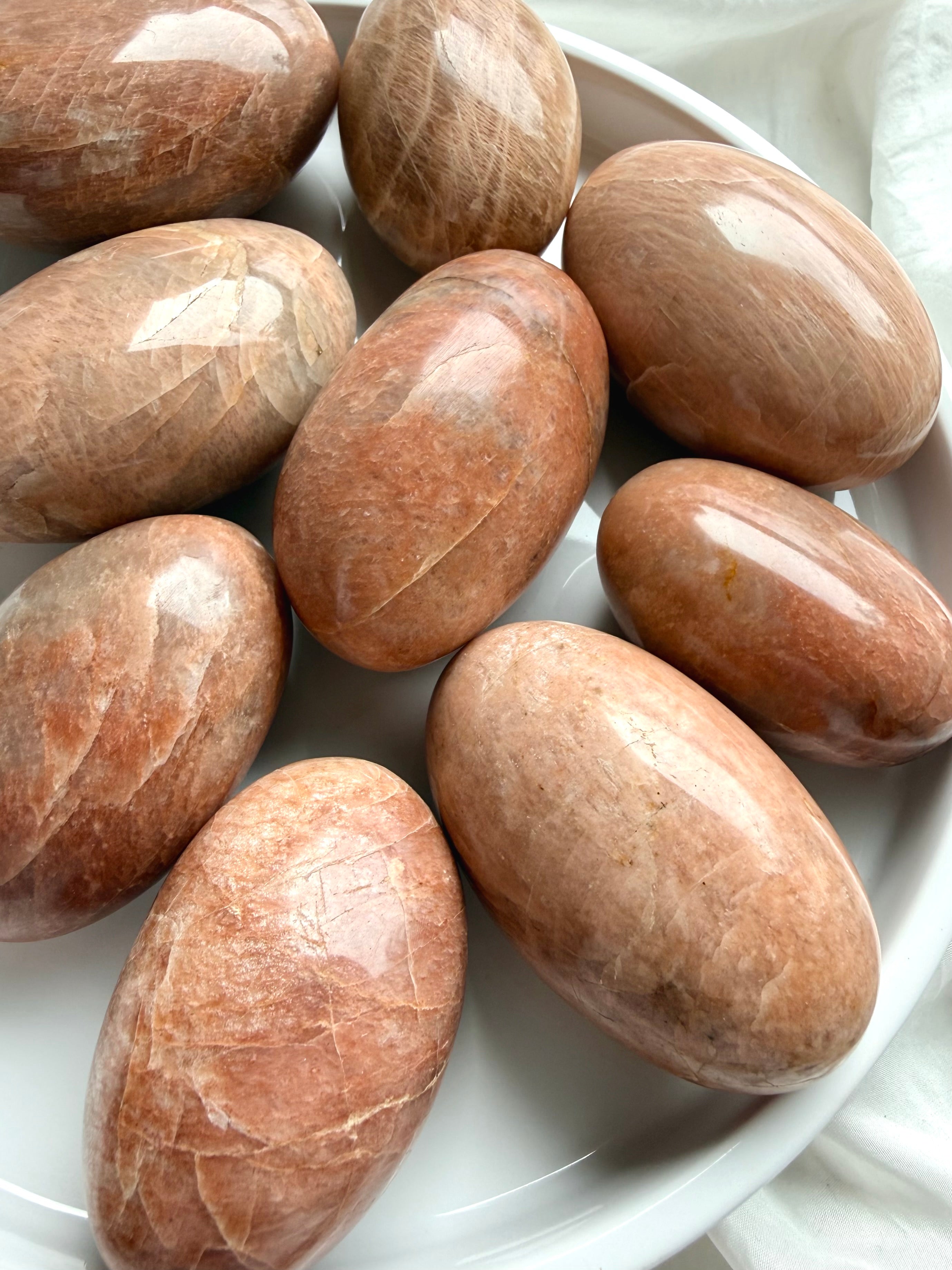 Large Peach Moonstone palm stones with warm peach and apricot tones on a white ceramic tray