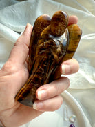 Golden Tiger’s Eye angel carving held in hand to show size and polished surface detail