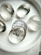 clear quartz palm stones on white tray with brand card beneath stone showing high clarity and natural inclusions