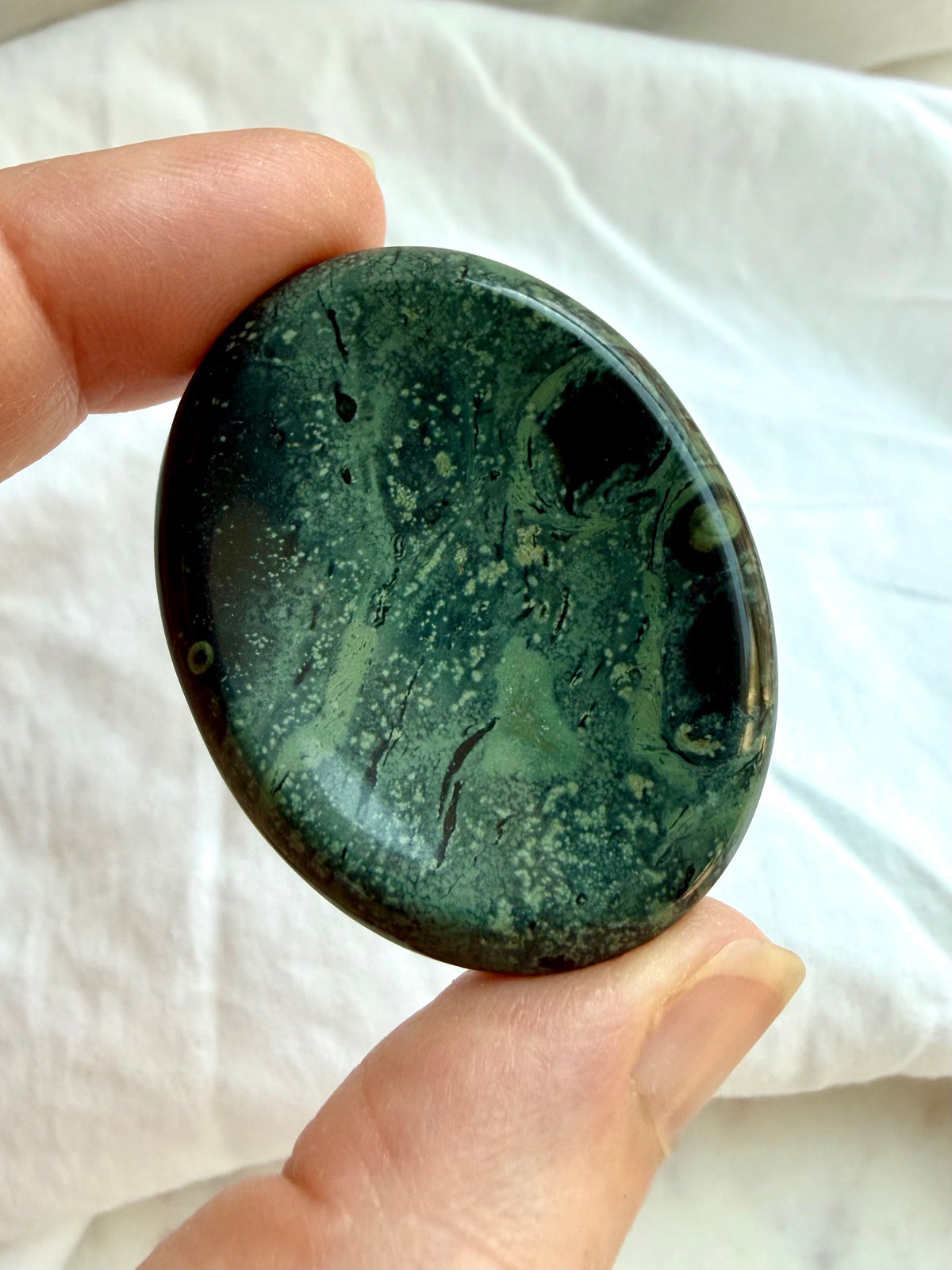 Kambaba Jasper worry stone held between fingers showing smooth oval shape, polished surface, and natural green patterning