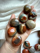 Small Polychrome Jasper pocket stones held in hand, showing rounded shapes, colorful natural banding, and polished surfaces