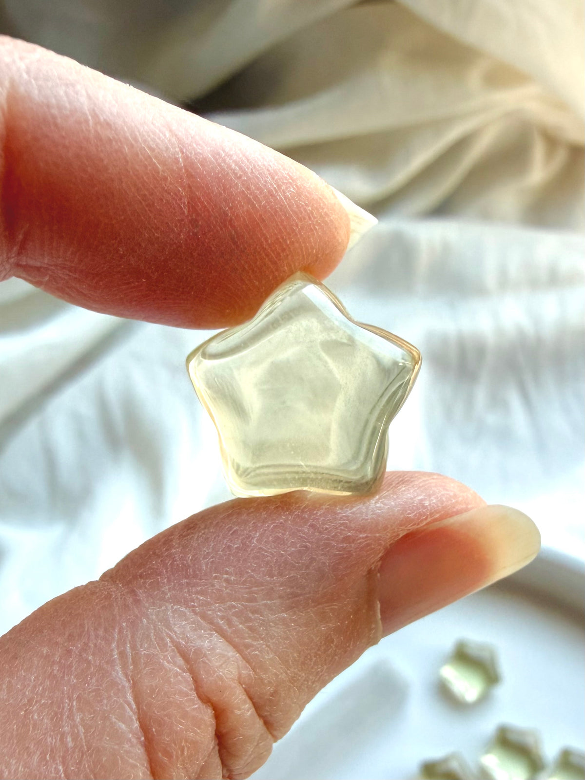 Mini Lemon Citrine star held between fingers showing its tiny size, translucence, and polished finish