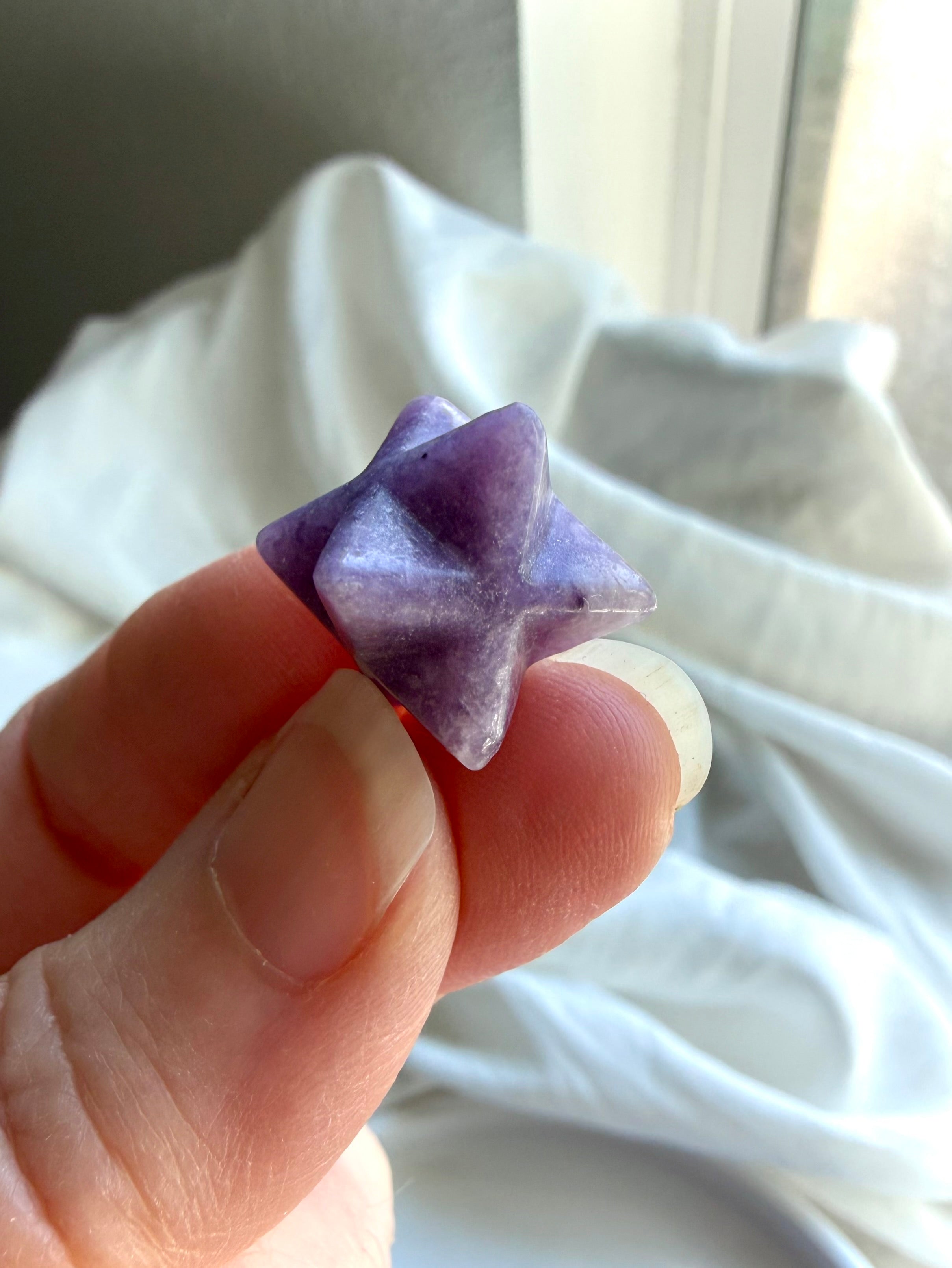 lepidolite merkaba star held between fingers, polished mini crystal for stress relief, intuition and inner peace