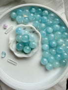 Aquamarine mini blue crystal balls styled on marble dish – soothing March birthstone spheres