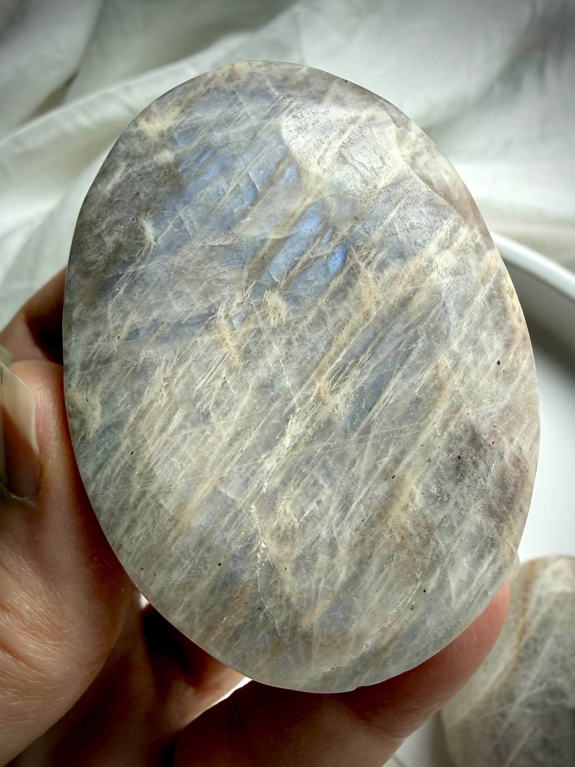 oval belomorite moonstone palm stone with silky silver flash and natural texture in hand