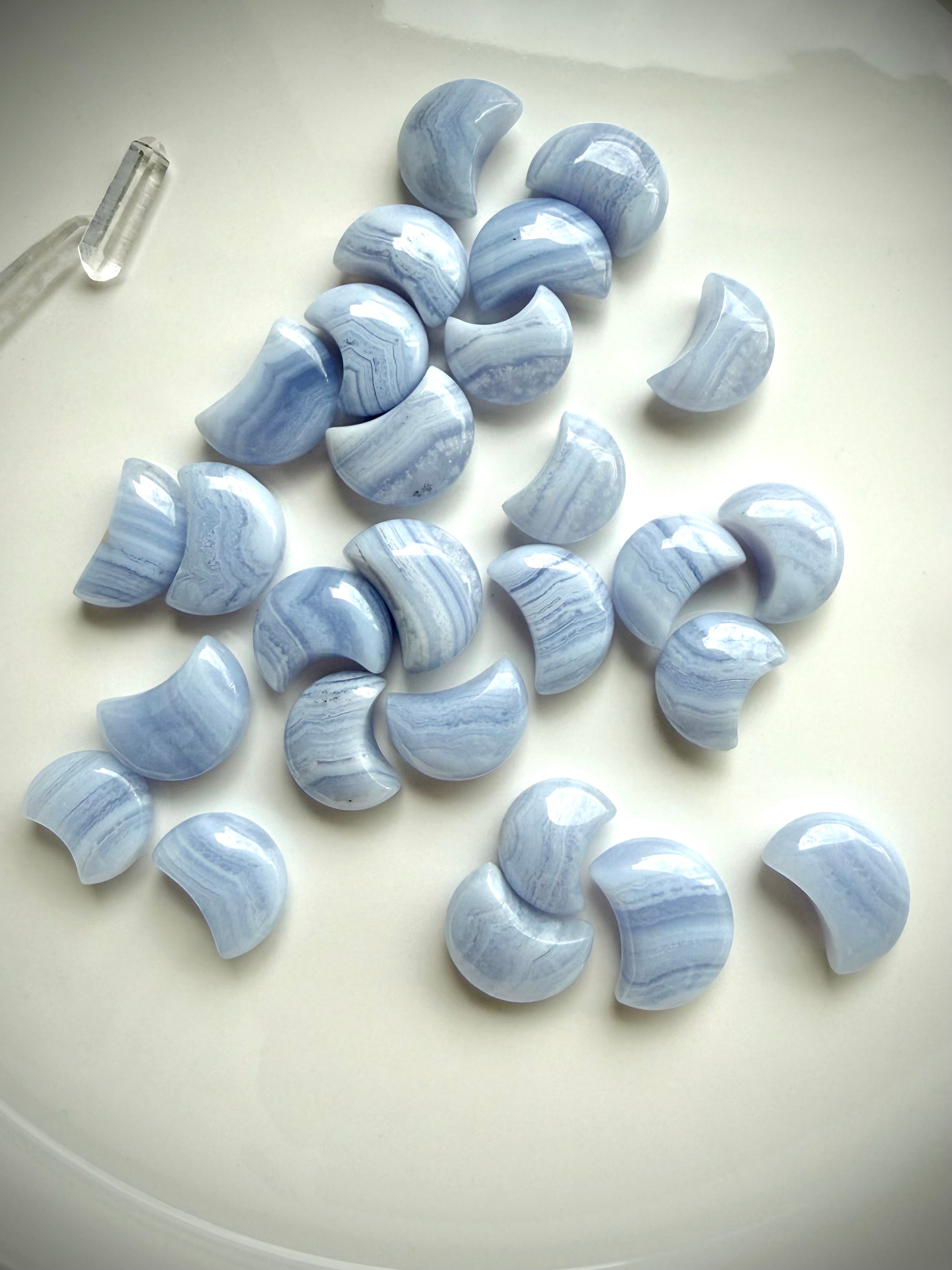 Assorted Blue Lace Agate crescent moon carvings arranged on a white ceramic plate with soft natural light
