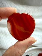 Polished Carnelian heart worry stone with bold red-orange agate banding for creativity, motivation and confidence