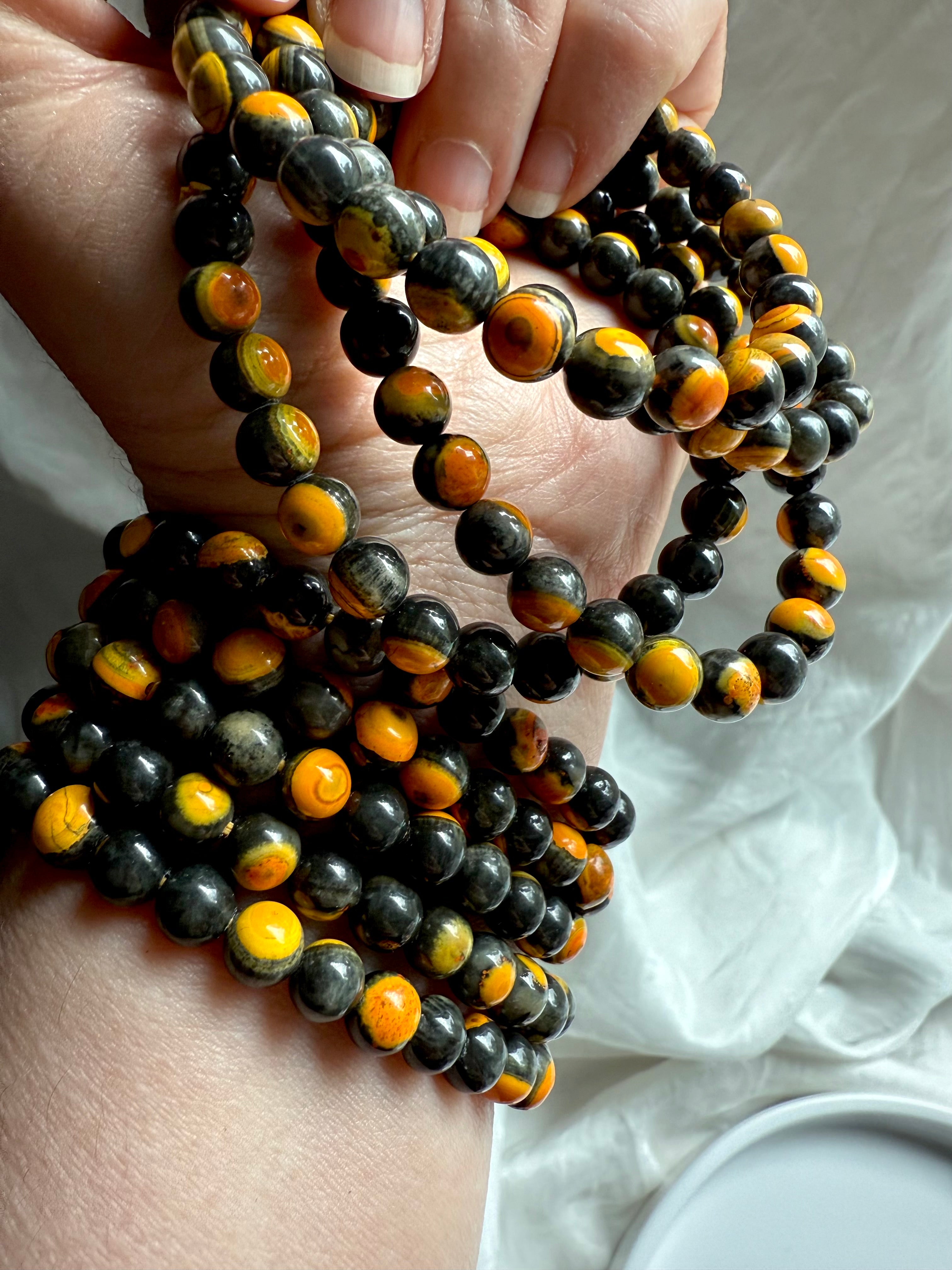 Wrist shot of multiple bumblebee jasper bracelets layered with faceted black crystal beads, energizing solar plexus bracelet stack for confidence and grounding