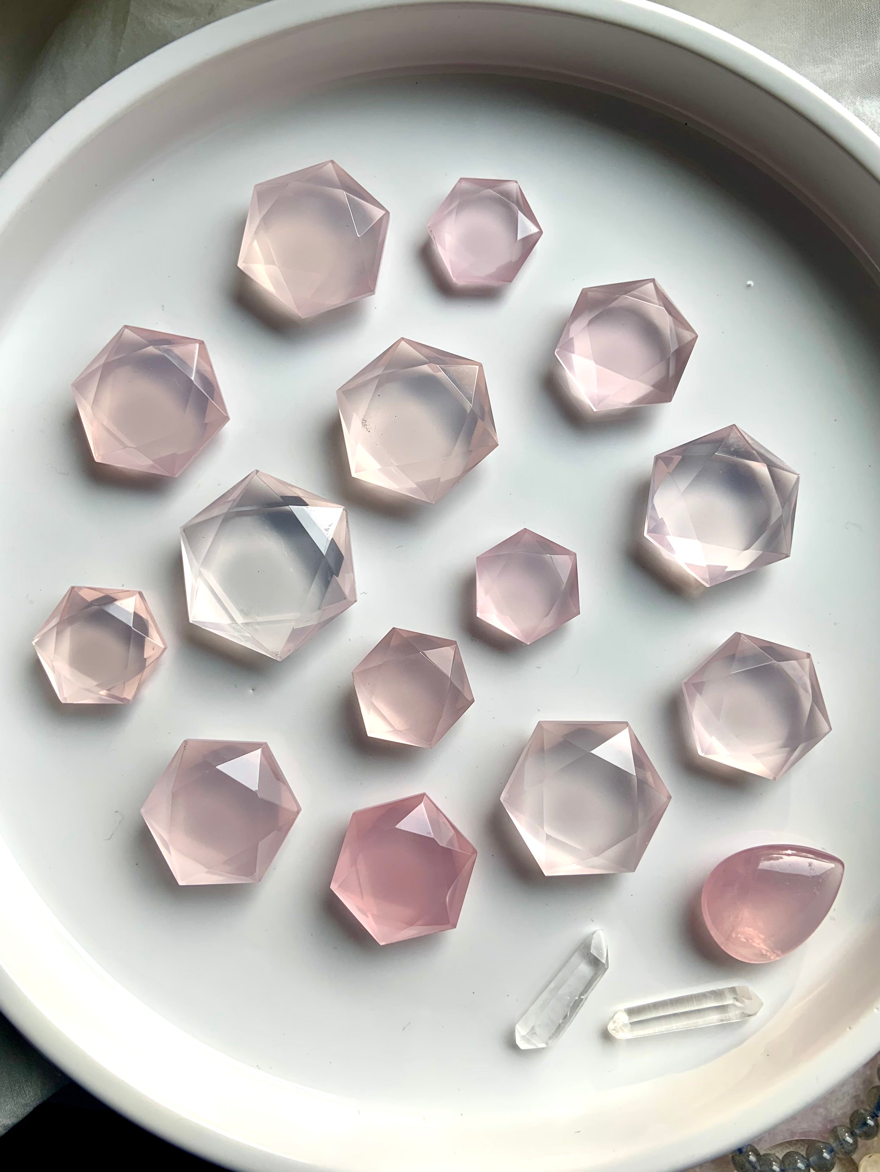Flatlay of faceted Rose Quartz hexagon crystals with clear quartz points, translucent pink sacred geometry gems for love and meditation