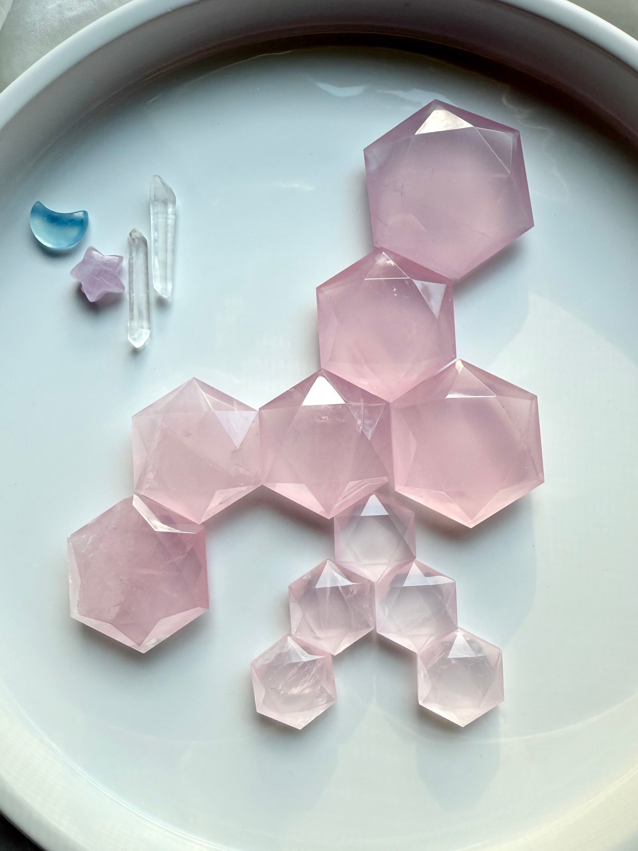Faceted rose quartz hexagon crystals in multiple sizes displayed in a honeycomb pattern on a white tray, heart chakra stones for love and healing.