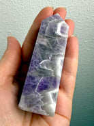 Polished Dream Amethyst crystal tower held in hand, showing its size, lavender purple coloring and distinctive white quartz chevrons