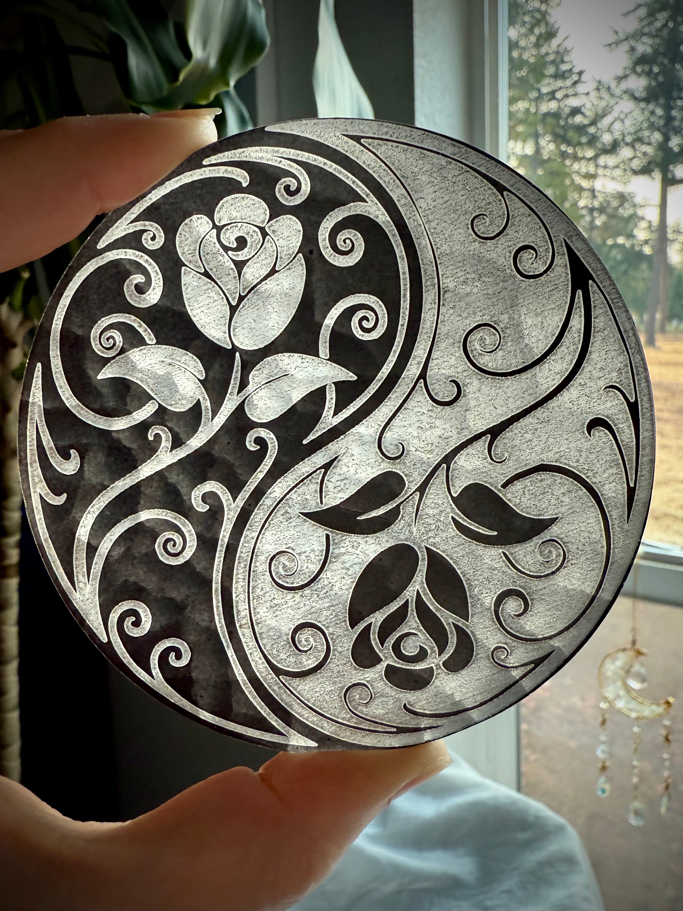 Selenite charging plate with yin yang rose design held to light, showing translucence and etched detail