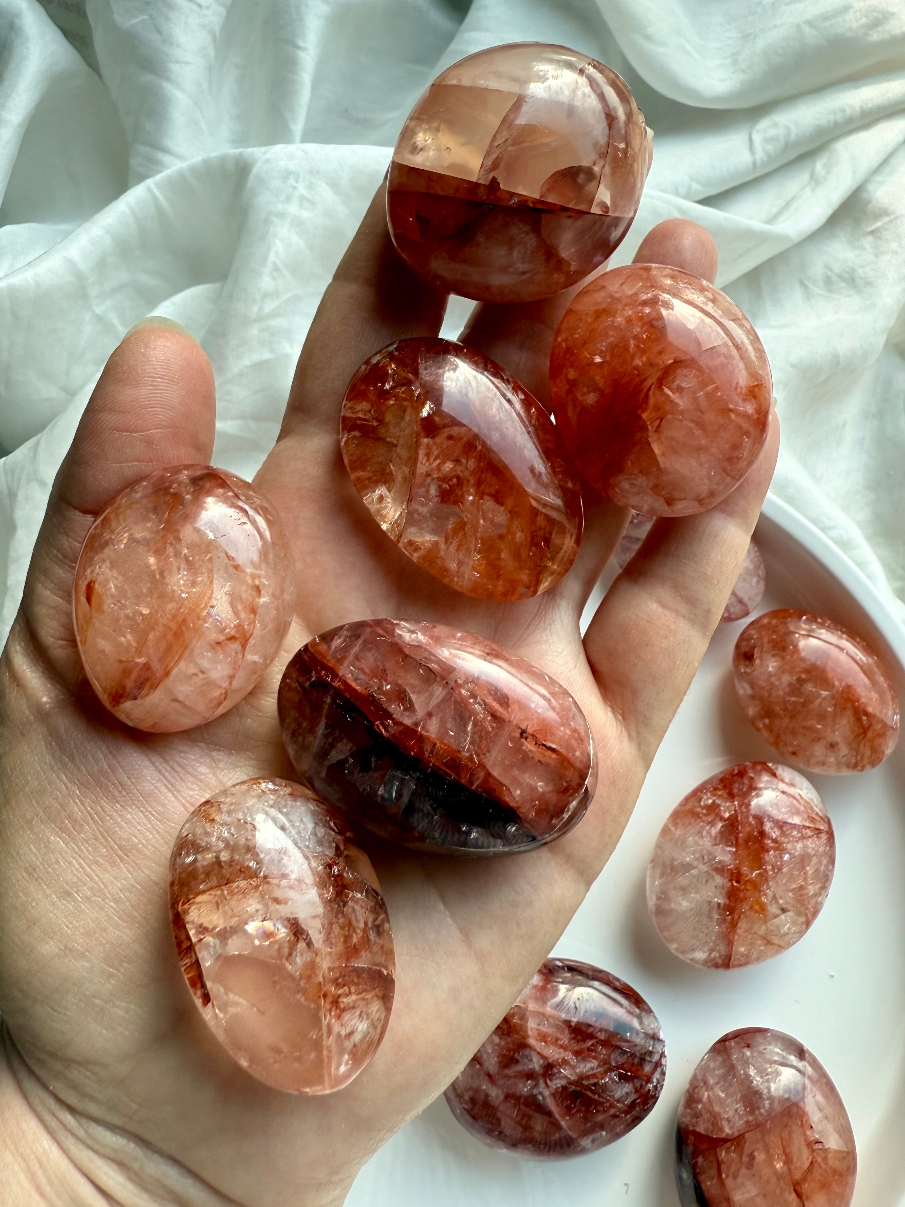 Hand holding polished Fire Quartz palm stones showing natural hematite streaks and grounding energy patterns