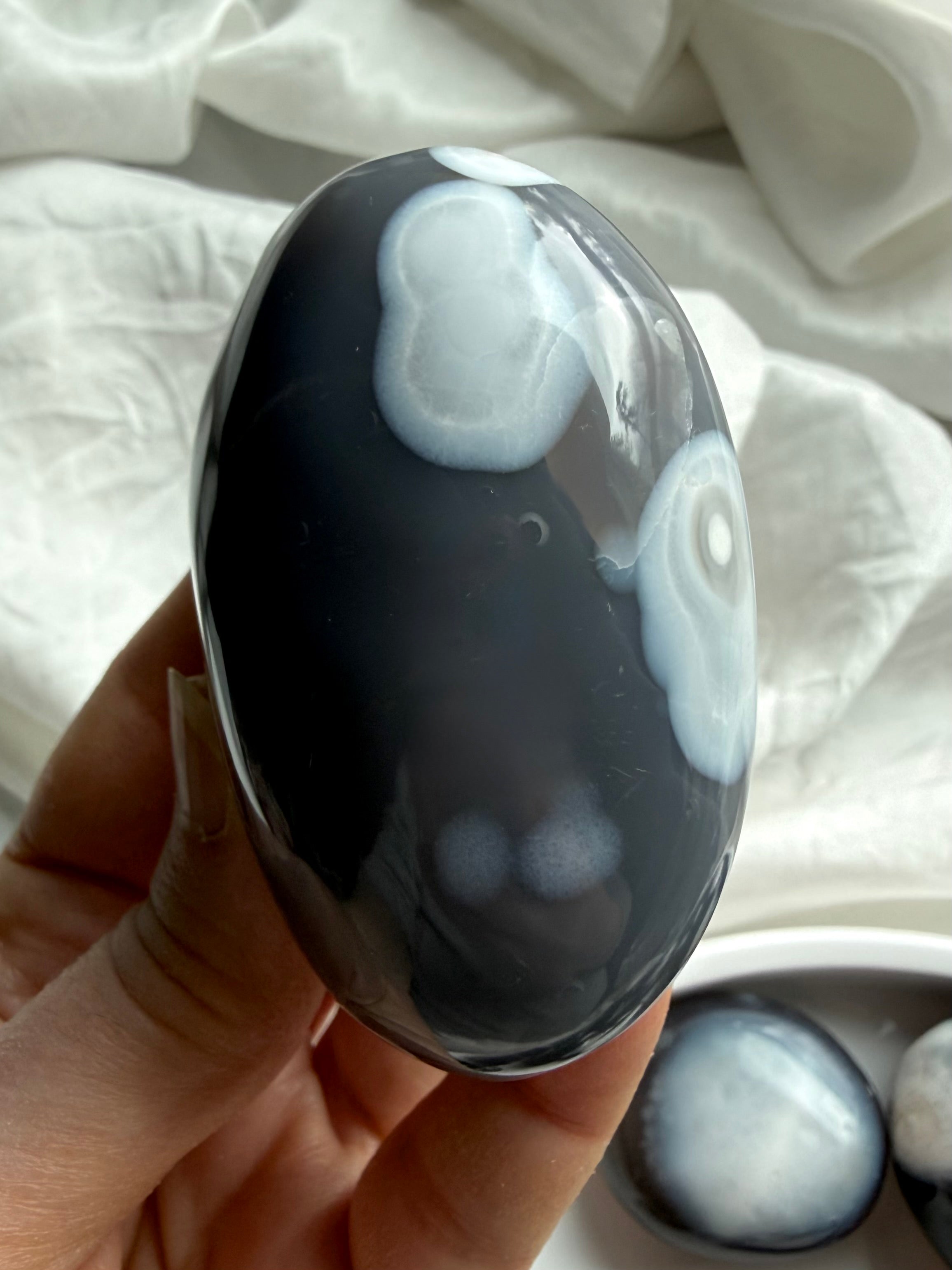 Close-up of Orca Agate palm stone with flowing gray and white agate layers, a grounding crystal for forgiveness and balance
