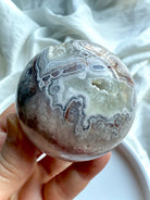 Banded Agate sphere with striking concentric patterns and natural druzy cavity, held in hand on white background