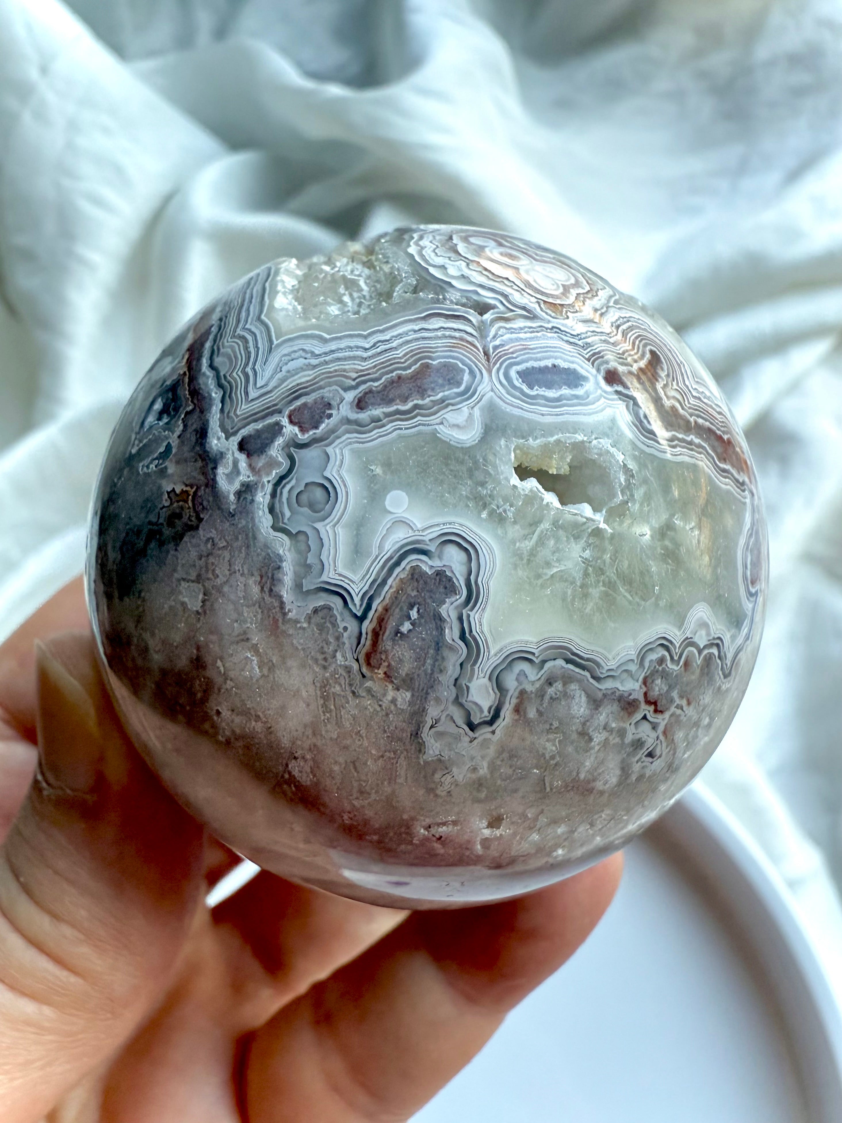 Banded Agate sphere with striking concentric patterns and natural druzy cavity, held in hand on white background