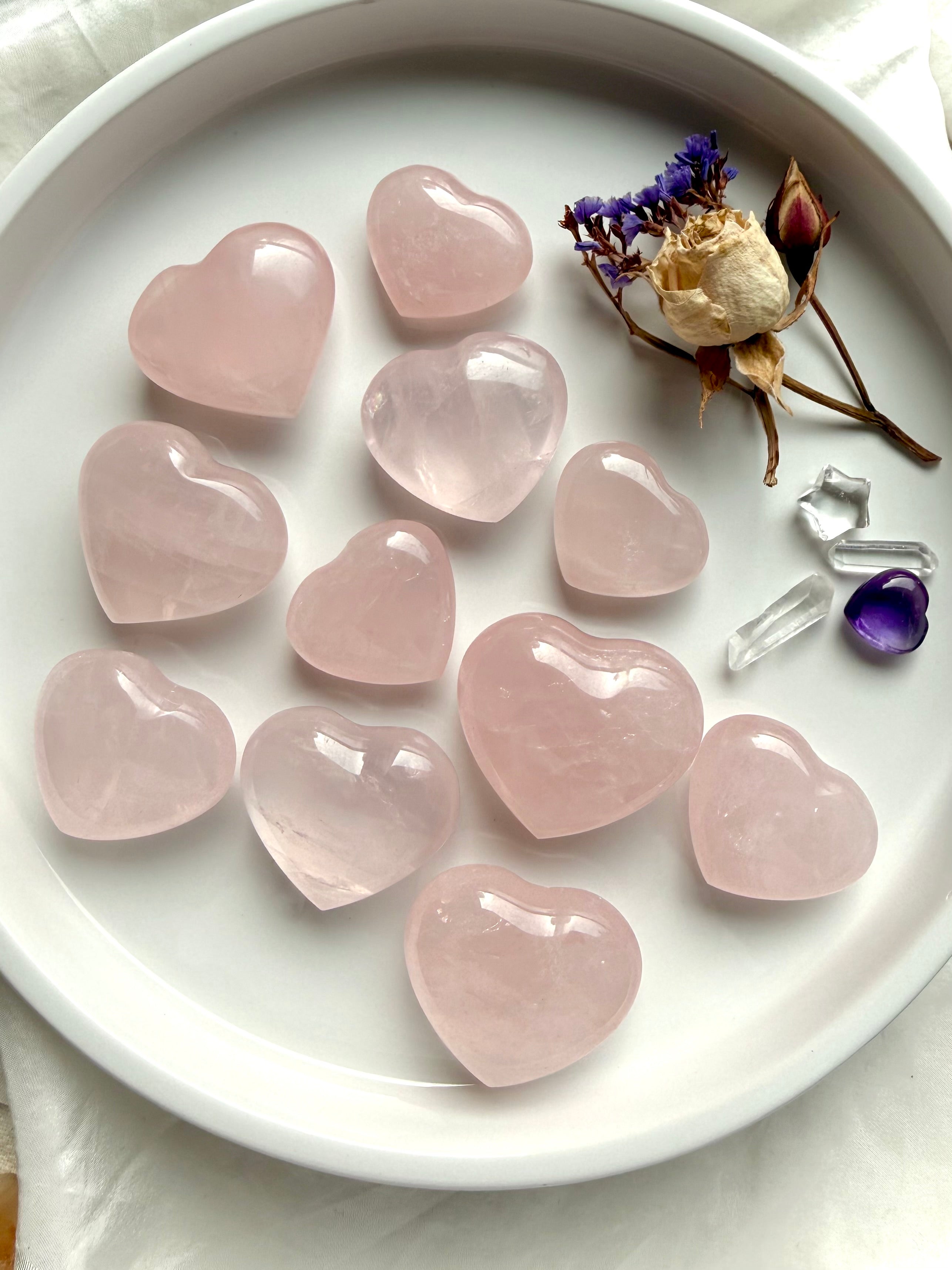 Rose quartz hearts on white tray with dried flowers and crystals, polished pink heart chakra stones for love and healing