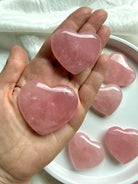 Palm-sized Rose Quartz hearts held in hand, polished healing crystals associated with love, compassion and the Heart Chakra