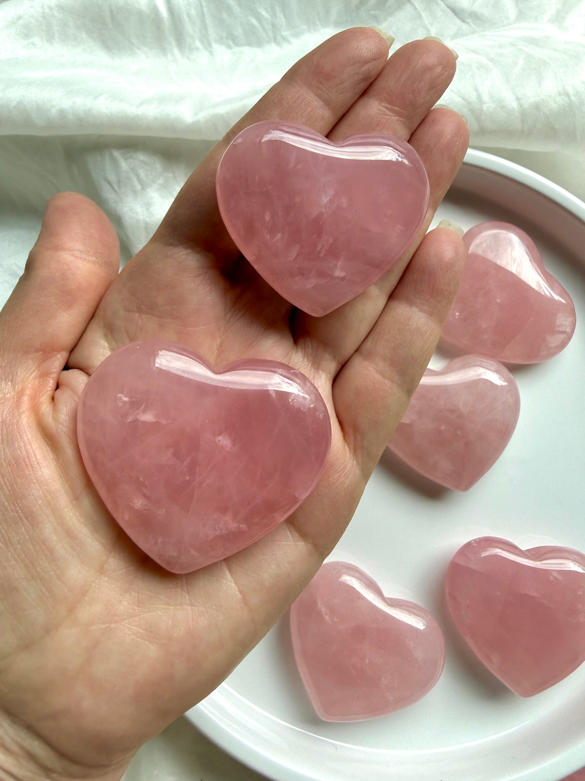Palm-sized Rose Quartz hearts held in hand, polished healing crystals associated with love, compassion and the Heart Chakra