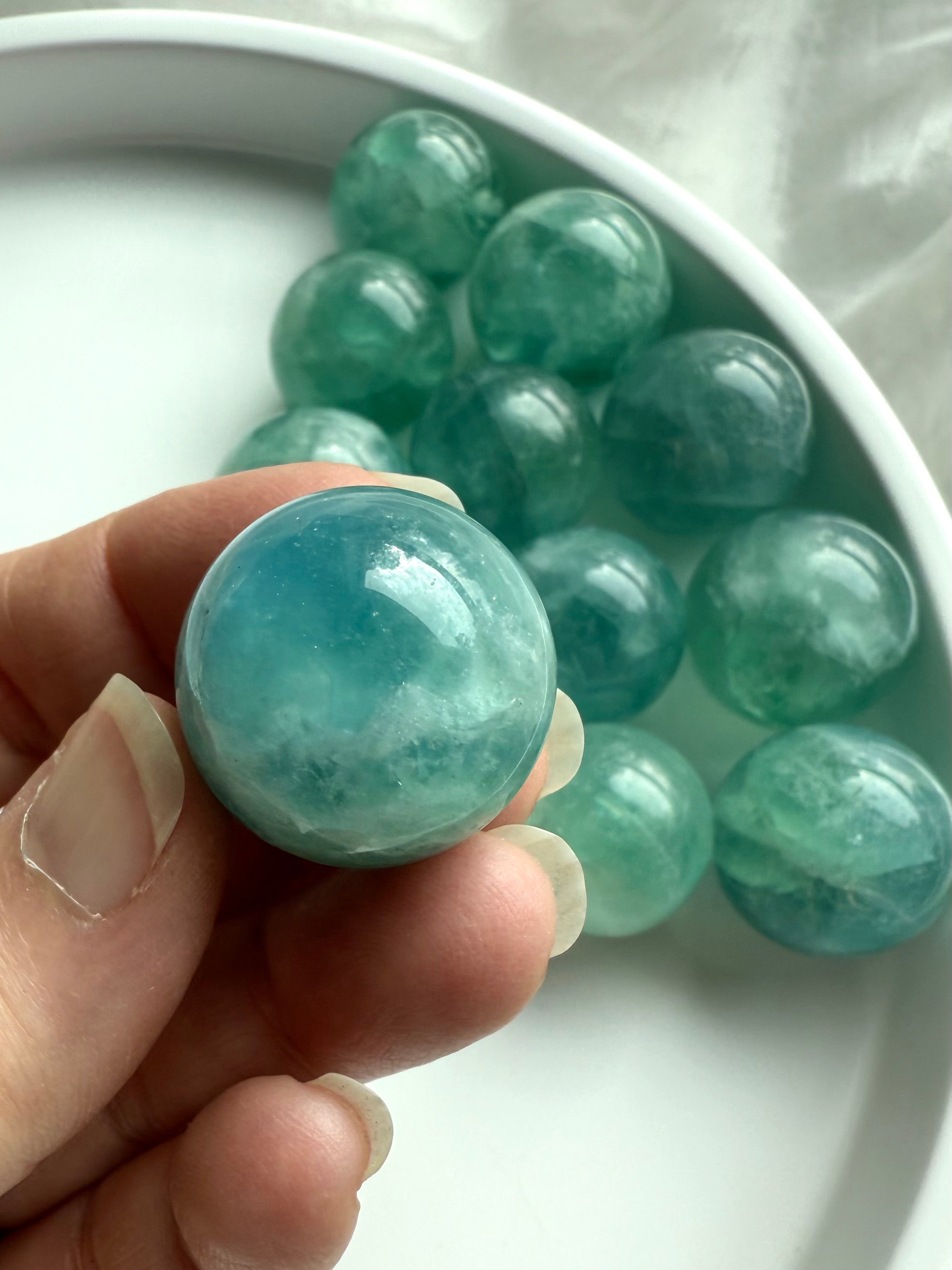 Hand holding a mini aqua teal Fluorite sphere with swirling translucence, rare crystal for calm and spiritual focus.