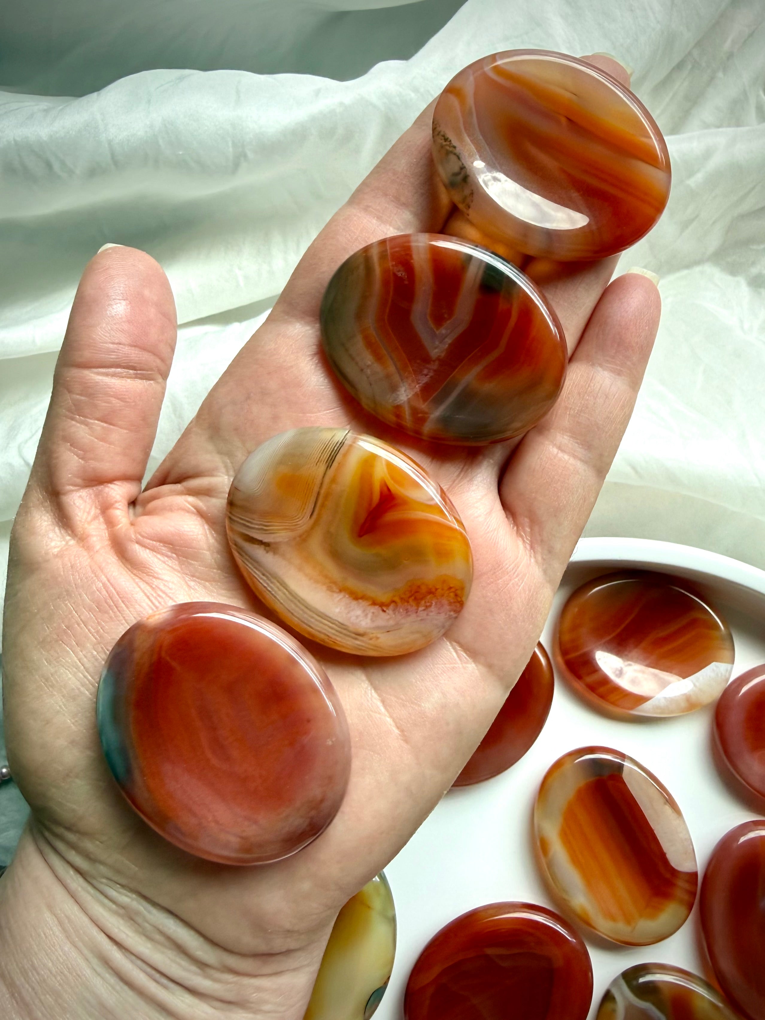Oval Carnelian worry stones held in hand showing polished thumb indentations and natural red-orange Agate patterns