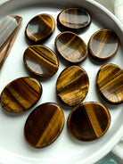 group of tiger’s eye worry stones scattered on marble surface, polished crystals for grounding stability and energy protection