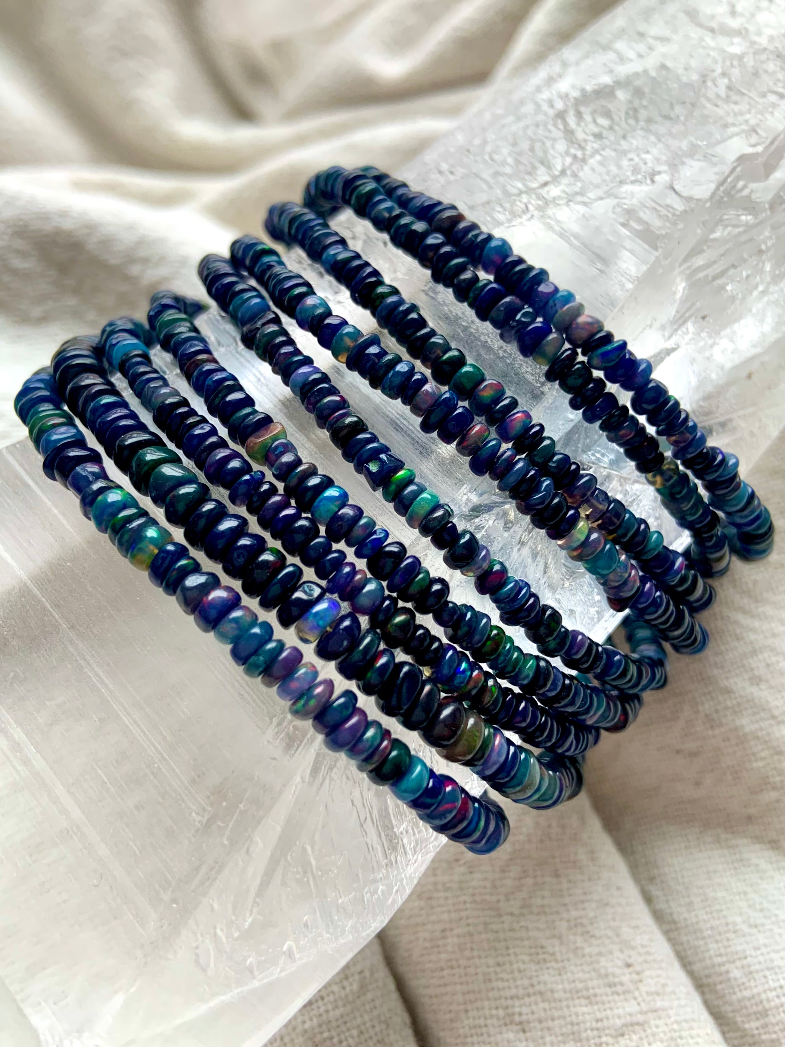 Bracelets draped over a quartz crystal — Genuine Black Opal bead bracelet with rainbow flash — sterling silver October birthstone jewelry gift.