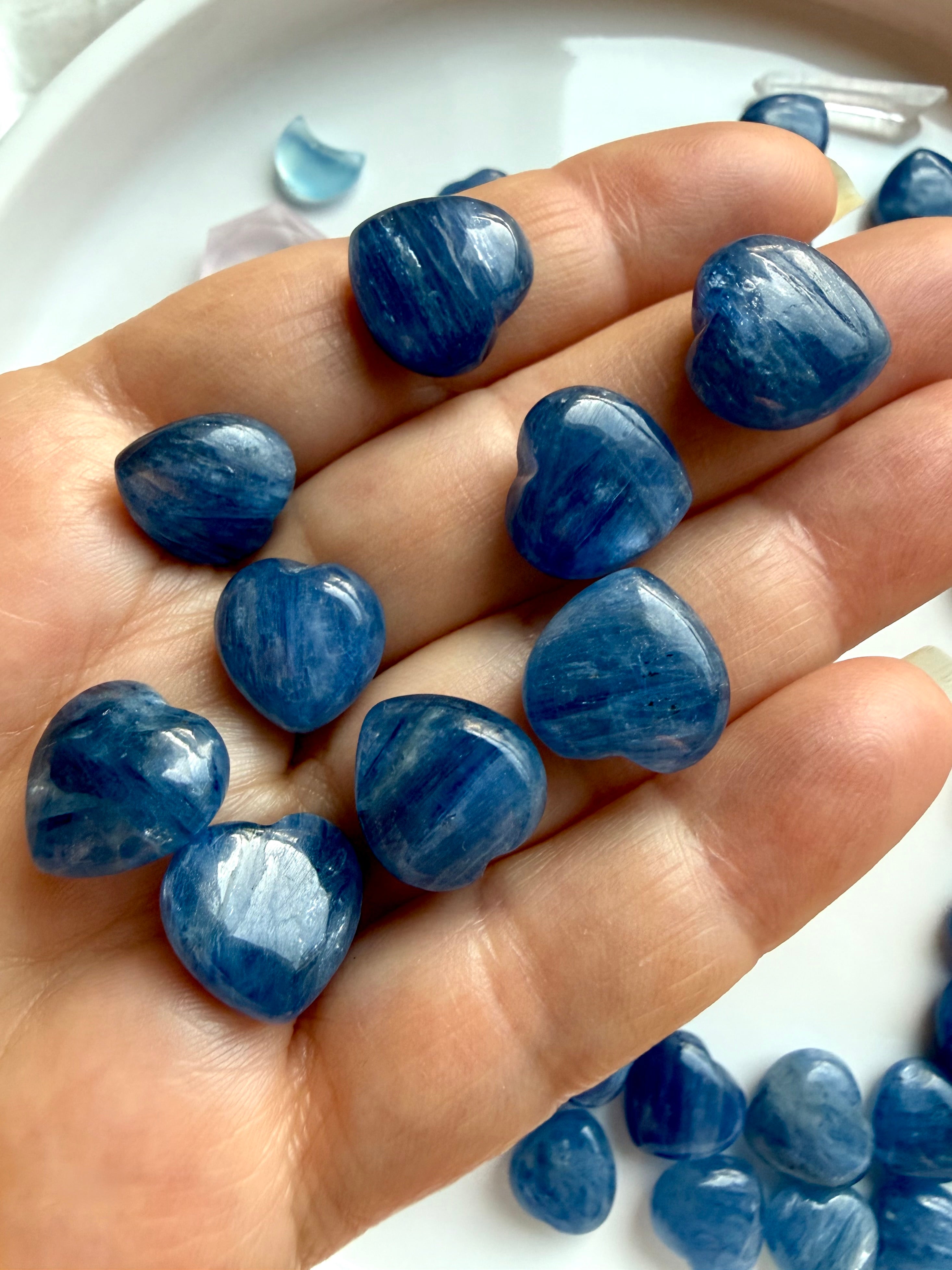 Mini Blue Kyanite heart crystals held in hand showing natural silvery blue shimmer and quartz inclusions, throat chakra healing stones