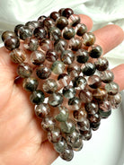 Hand holding Garden Quartz bracelets with scenic mineral formations inside transparent quartz spheres