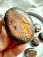 Close-up of Peach Sunset Labradorite palm stone showing orange, pink, and golden labradorescence