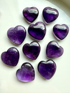 Polished Amethyst hearts arranged on a white dish — soothing healing crystals for intuition, meditation, and crown chakra activation.