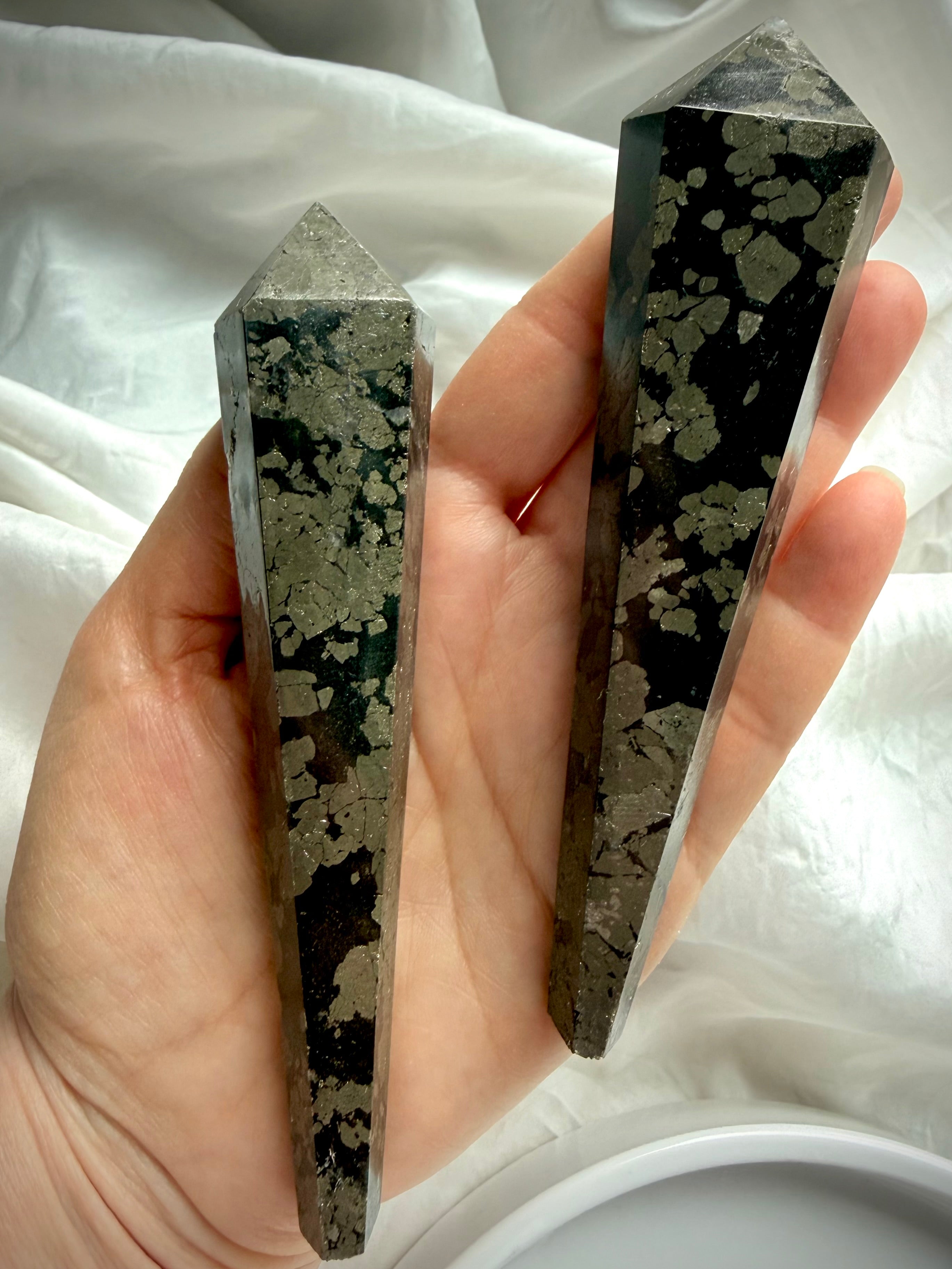 two pyrite wands in black matrix held in hand showing polished crystal points and natural gold pattern