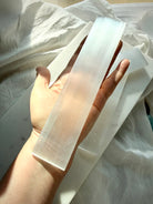 Selenite crystal cleansing wand resting across an open hand, highlighting its translucent white glow and polished rectangular shape