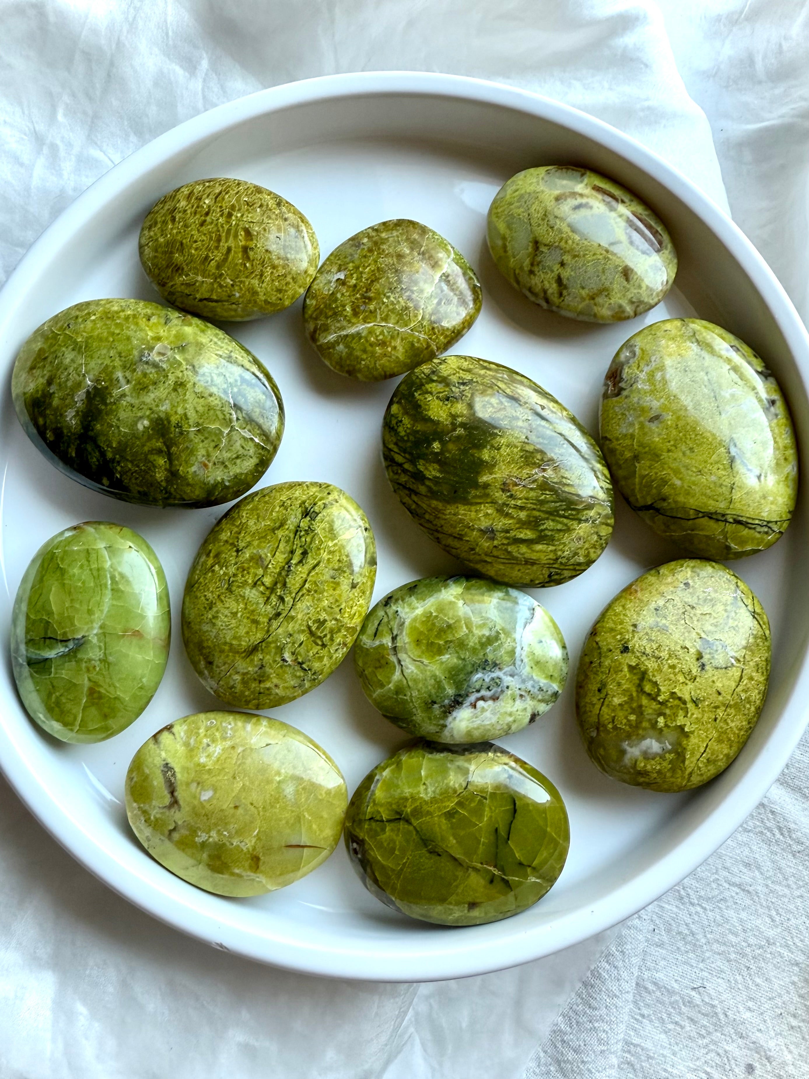 Flatlay of Green Opal palm stones on a white plate, showing irregular oval shapes, natural variations, and luminous yellow-green hues.