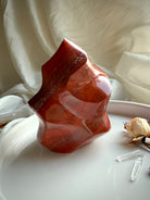Red Ocean Jasper crystal flame displayed on a white tray with dried flowers and quartz points.
